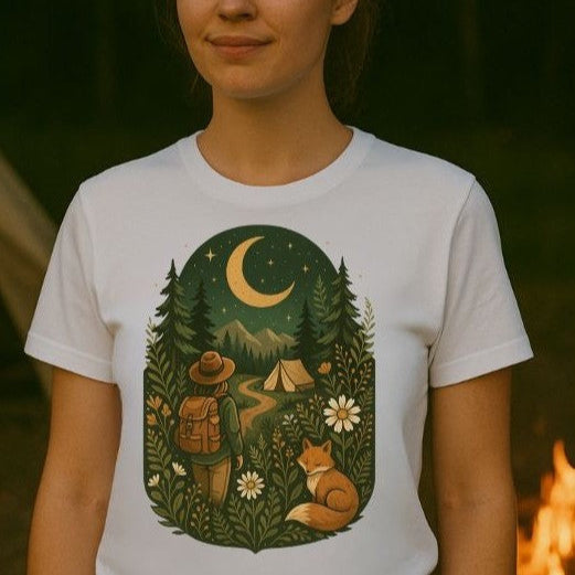 Person wearing a white t-shirt with a nature-themed graphic design featuring a crescent moon, trees, a fox, and a camper.